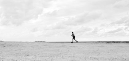 A lone runner traverses a vast, empty Brazilian beach under dramatic cloudy skies in black and white.