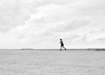 A lone runner traverses a vast, empty Brazilian beach under dramatic cloudy skies in black and white.