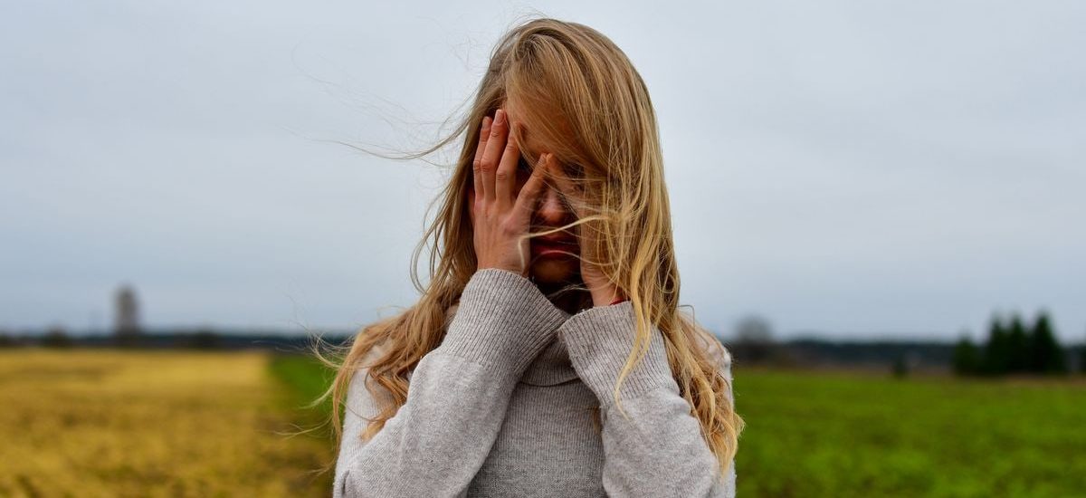 A woman with blonde hair in a sweater stands in a windy meadow in Harju County, Estonia.