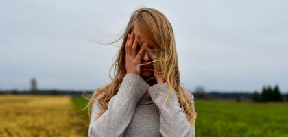 A woman with blonde hair in a sweater stands in a windy meadow in Harju County, Estonia.