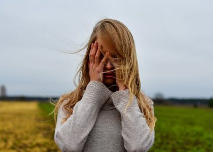 A woman with blonde hair in a sweater stands in a windy meadow in Harju County, Estonia.